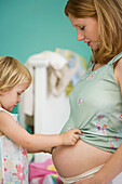 Little girl looking at mother's pregnant belly
