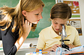 Boy looking through microscope, teacher watching