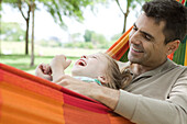 Father and daughter relaxing together in hammock, both laughing