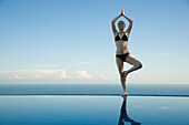 Woman standing in tree pose on edge of infinity pool