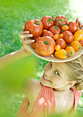 Young woman holding up bowl of tomatoes, smiling at camera
