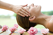 Woman lying on deck, surrounded with flowers, having head massage