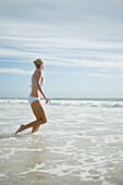 Young woman in bikini, running in surf