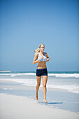 Young woman running on beach, front view