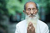 Elderly man in traditional Chinese clothing, hands clasped in prayer
