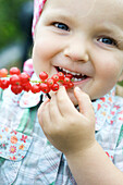 Little girl eating red currants off stem, smiling at camera