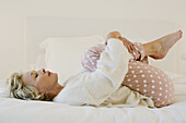 Mature woman lying on bed in fetal position