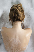 Woman relaxing in bubble bath, rear view
