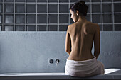 Frau sitzt auf dem Rand einer Badewanne, Rückansicht