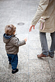 Father reaching for toddler's hand on sidewalk, cropped