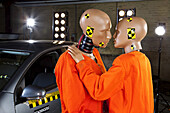 Two crash test dummies next to a car in a crash test laboratory about to kiss