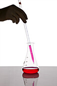 A lab technician using a dropper to put fluid into a beaker, close-up of hand