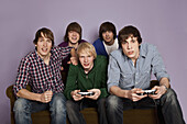 Two teenage boys playing a video game while their friends cheer them on