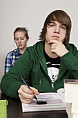 A teenage boy thinking in a classroom, girl in background