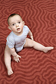 A baby boy sitting on a patterned carpet