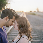 A young couple touching foreheads near railroad track