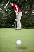 A female golfer putting, golf ball at edge of hole