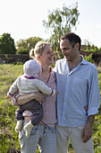 A man and a woman holding a baby standing in their backyard