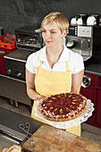 A sales clerk holding a fruit and nut tart