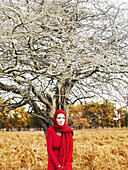 A woman wearing a bright red dress and scarf standing under a leafless tree in nature