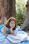 Girl lying on blanket in park with book