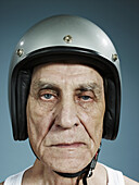 A headshot of a frowning senior man wearing a crash helmet