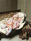 Baby on embroidered blankets on wooden chest