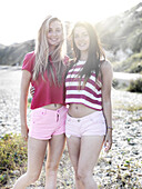 Two smiling young women with their arms around each other standing on a beach