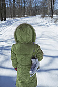A young girl standing on a snowy road with an ice skate slung over her shoulder