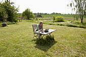 A woman with a laptop sitting at a table in her back yard, rural setting