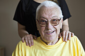 A senior man in a nursing home, hands on his shoulders, focus on him
