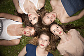 Five female friends lying in the grass in a circle looking sensually at the camera