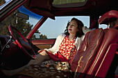A pretty rockabilly woman sitting in the front seat of a vintage car