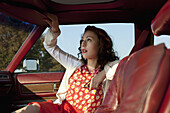 A pretty rockabilly woman pulling a sun visor down in a vintage car