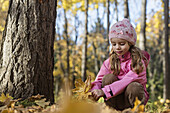A young girl picking up autumn leaves in a wooded area