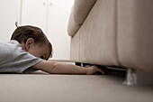A boy reaching under a sofa to retrieve something