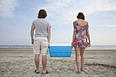 A young couple carrying a cooler together on the beach