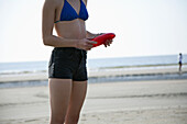 A woman holding a plastic disc at the beach, midsection