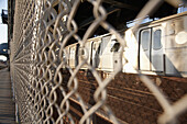 Train seen through wire fence which separates the pedestrian walkway on Manhattan Bridge