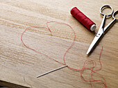 A spool of red thread, scissors, thread needle and thread shaped like a heart