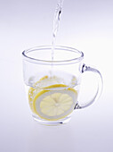 Water being poured in lemon tea over colored background