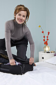 A woman trying to close an overflowing suitcase