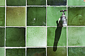 A tap on a green tiled wall