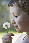 A boy holding a dandelion up to his nose
