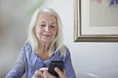 Senior woman text messaging through smart phone at home