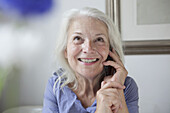 Happy senior woman looking up while answering mobile phone at home