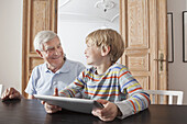 Happy senior man looking at grandson with digital tablet at home