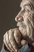 Close-up side view of thoughtful senior man with hand on chin over brown background