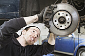 Smiling male worker repairing car in auto repair shop