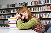 A girl takes a nap on a pile of books in a library